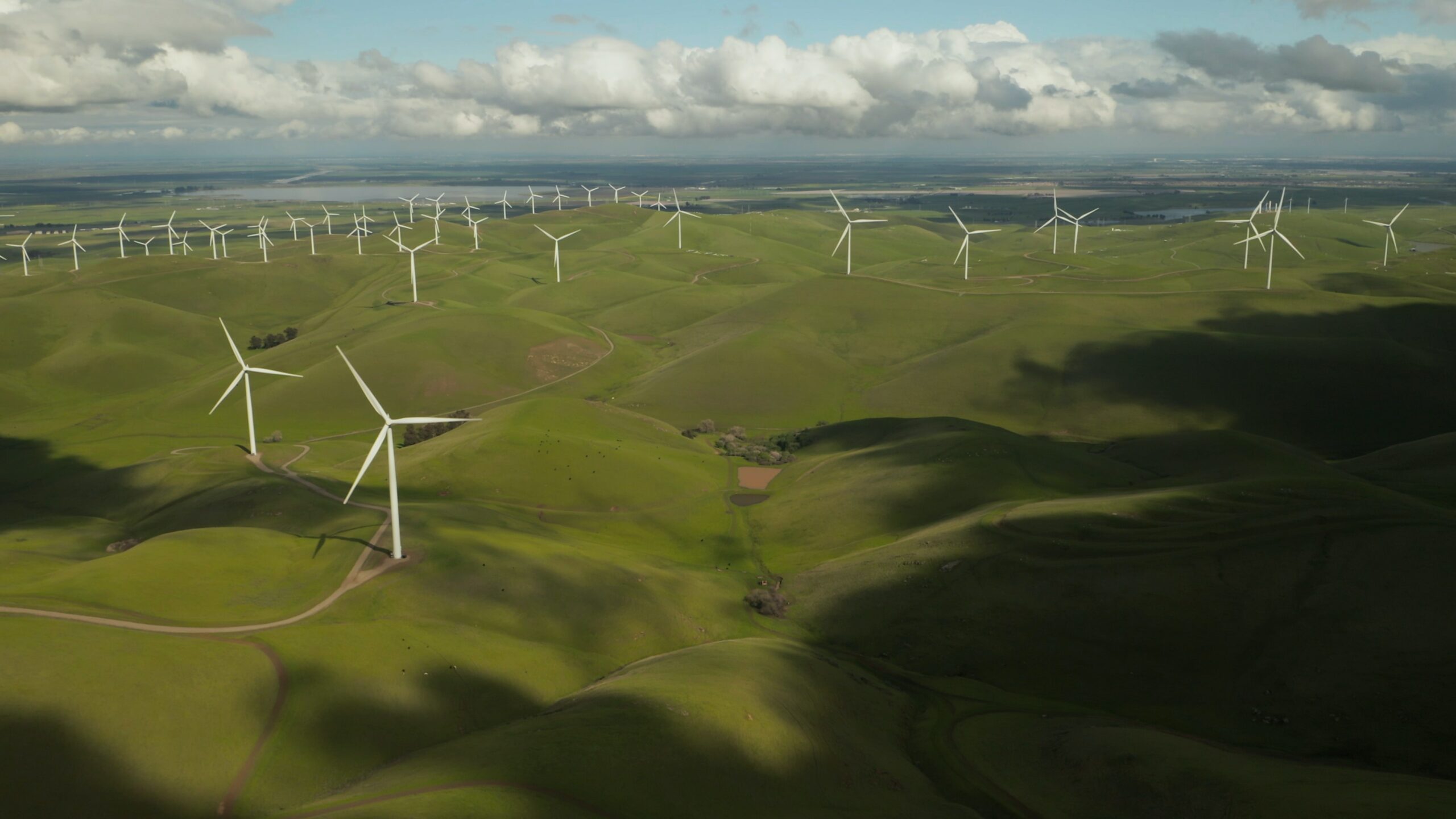 Wind mills in an open field with water in the background